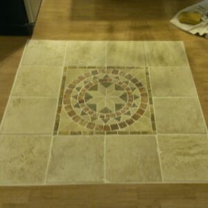 Custom tile floor inlay with a circular mosaic centerpiece design in warm tones, set against a wood floor.