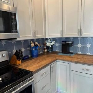 Modern kitchen featuring white cabinetry, butcher block countertops, and a floral-patterned blue backsplash.