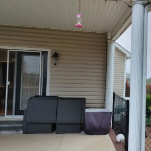 A home's covered porch with outdoor wicker furniture and a hummingbird feeder hanging above.