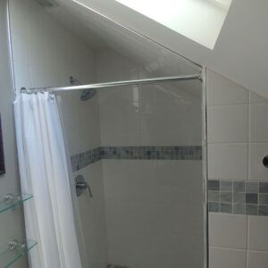 A sleek, newly remodeled bathroom featuring white tiles with a blue accent stripe and skylight.